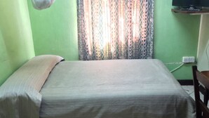 A single bed with a plain bedspread in a room with green walls and a patterned curtain. - Sooper Guest House (Kisumu)