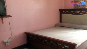 A single bed with a wooden frame and headboard, a television on a stand, and a power outlet on the wall. - Sooper Guest House (Kisumu)