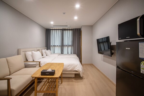 Una habitación de hotel moderna con cama, sofá, mesa de madera, televisor y refrigerador.
