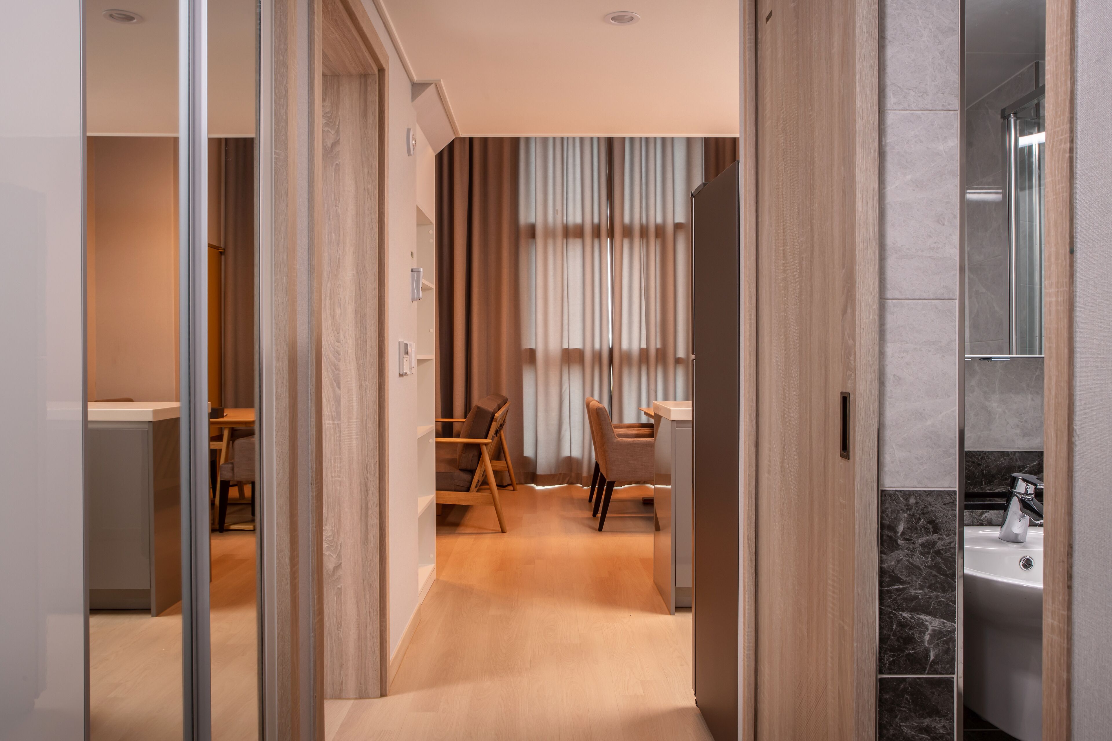 A modern hotel room with a wooden floor, a dining area with a table and chairs, and a bathroom with a marble sink.