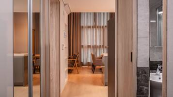 A modern hotel room with a wooden floor, a dining area with a table and chairs, and a bathroom with a marble sink.