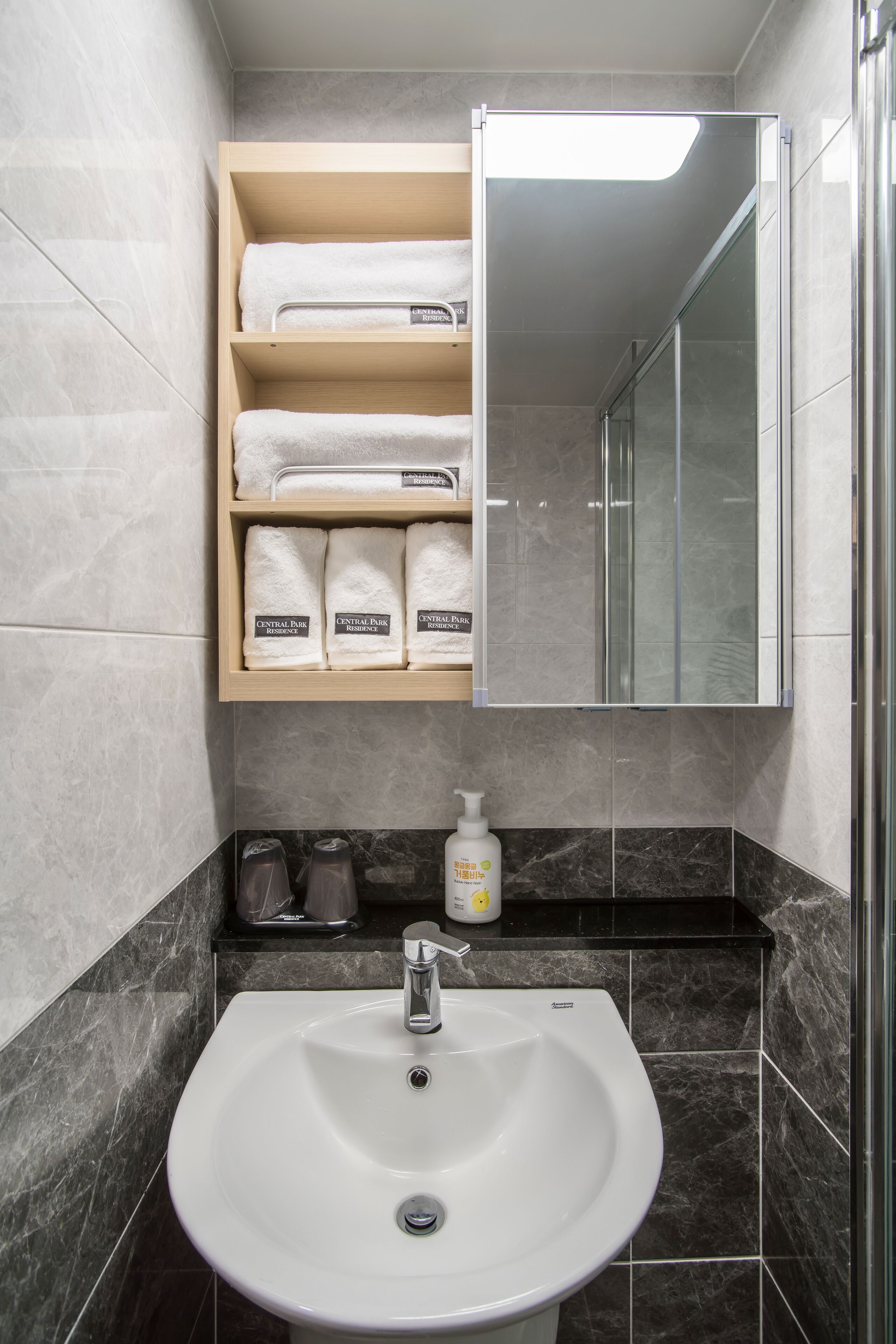 Un baño con lavamanos blanco, un espejo y un estante con toallas.