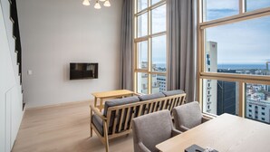 Un salon moderne avec une grande fenêtre, un canapé, une table à manger et un téléviseur fixé au mur.