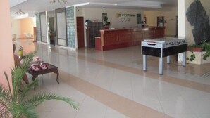 Un vestíbulo amplio con mostrador de recepción, una mesa de fútbol de mesa y una gran escultura de roca.