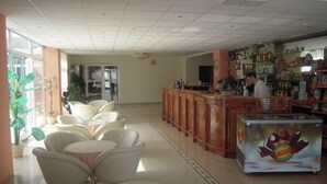 Vestíbulo de hotel con área de bar, asientos y un refrigerador con publicidad de bebidas.