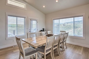 Zona pranzo con tavolo in legno e sei sedie, ampie finestre con tende e bocchetta di ventilazione a soffitto.