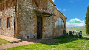 A rustic stone building with a large arched window and a small door, surrounded by a grassy area with outdoor seating. - Charming Tuscan Farmhouse (Arbia Asciano)