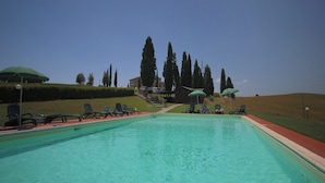 A swimming pool with lounge chairs and umbrellas, surrounded by trees and a building in the background. - Charming Tuscan Farmhouse (Arbia Asciano)