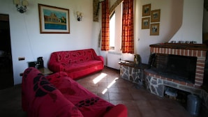 A cozy living room with a red sofa, a fireplace, and a painting on the wall. - Charming Tuscan Farmhouse (Arbia Asciano)
