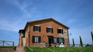 Una casa de ladrillo de dos pisos con una escalera de piedra que conduce a la entrada, un pequeño jardín y una cerca de metal en primer plano.