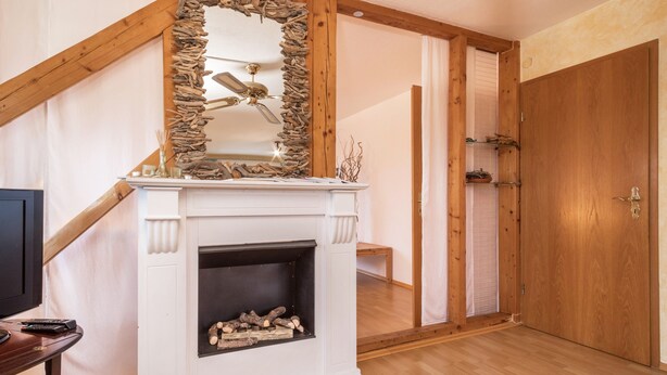 Una habitación con chimenea blanca, un espejo con marco de madera, una puerta de madera y una escalera.