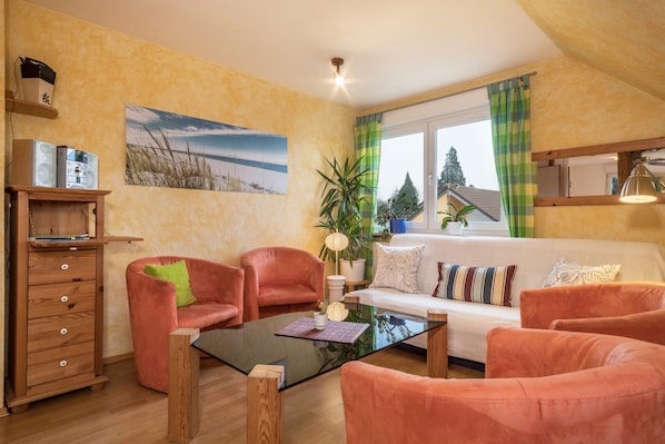 Un salon comprenant un canapé, deux fauteuils, une table basse, un meuble en bois, une plante et un tableau accroché au mur.