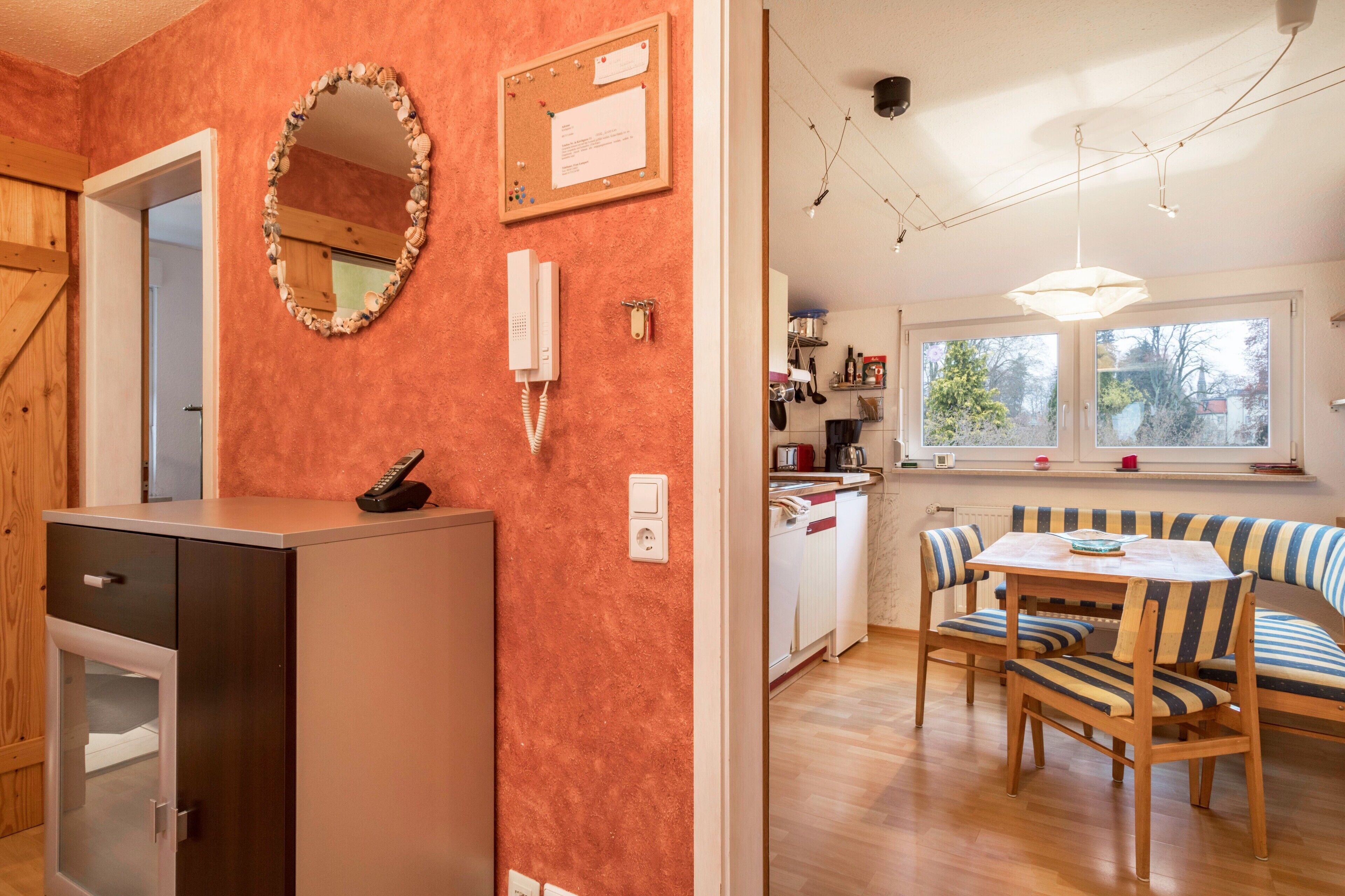 Een kleine keuken met een houten kastje, een telefoon en een prikbord.