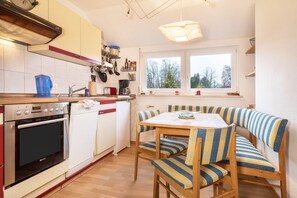 Une cuisine équipée d’un four encastré, d’un lave-vaisselle et d’un coin repas avec des chaises à rayures et une table.