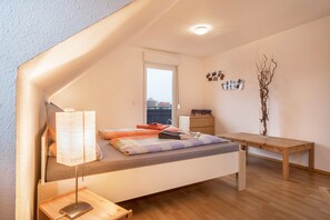Une chambre à coucher de taille modeste, comprenant un lit, une lampe de chevet, un bureau en bois et une petite table.