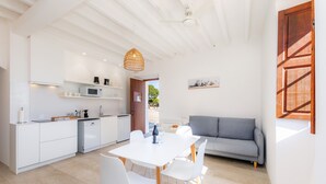 Eine moderne Küche mit weißen Schränken, einem Esstisch mit Stühlen und einem grauen Sofa in einem hellen Raum mit Holzbalken an der Decke.