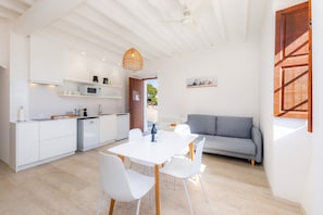 Une cuisine moderne avec des meubles blancs, une table à manger avec des chaises et un canapé gris dans une pièce lumineuse agrémentée de poutres en bois au plafond.