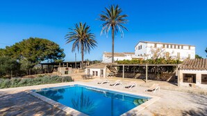 Ein Pool mit Liegestühlen, Palmen und einem weißen Gebäude im Hintergrund.