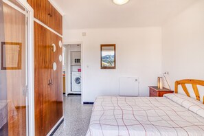 A bedroom with a bed, wooden wardrobe, a washing machine, a radiator, and a view of a mountain.