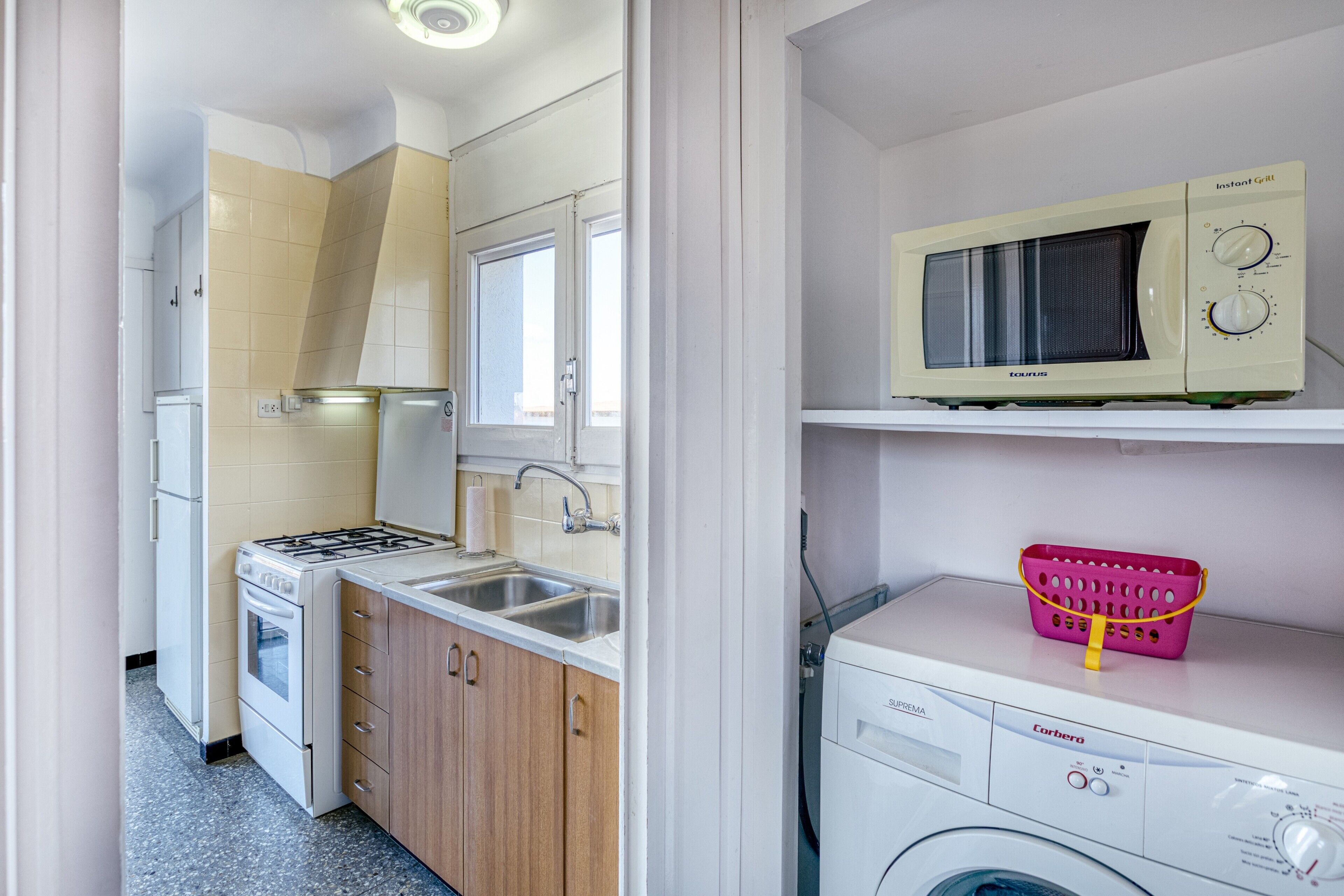 A compact kitchen with a stove, sink, and microwave, and a laundry area with a washing machine and a basket.