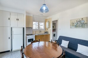 A compact kitchen with a dining table, a sofa, and a hanging light fixture.