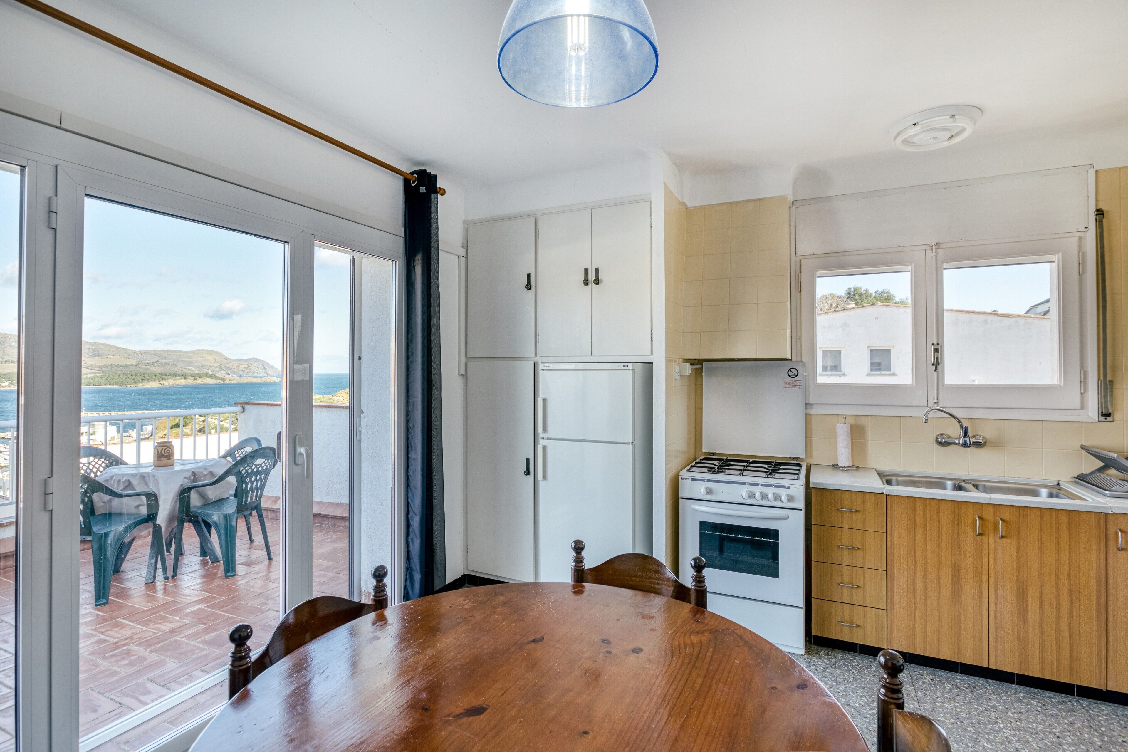 A kitchen with a stove, sink, and cabinets, a dining table with chairs, and a view of the sea through large windows.