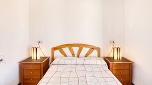 Une chambre à coucher avec une tête de lit en bois, deux tables de chevet avec des lampes, un lit recouvert d’une couverture à carreaux et une table de nuit dotée d’une prise électrique.