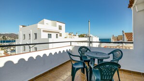 Ein Balkon mit Tisch und Stühlen, Blick auf das Meer und Gebäude im Hintergrund.