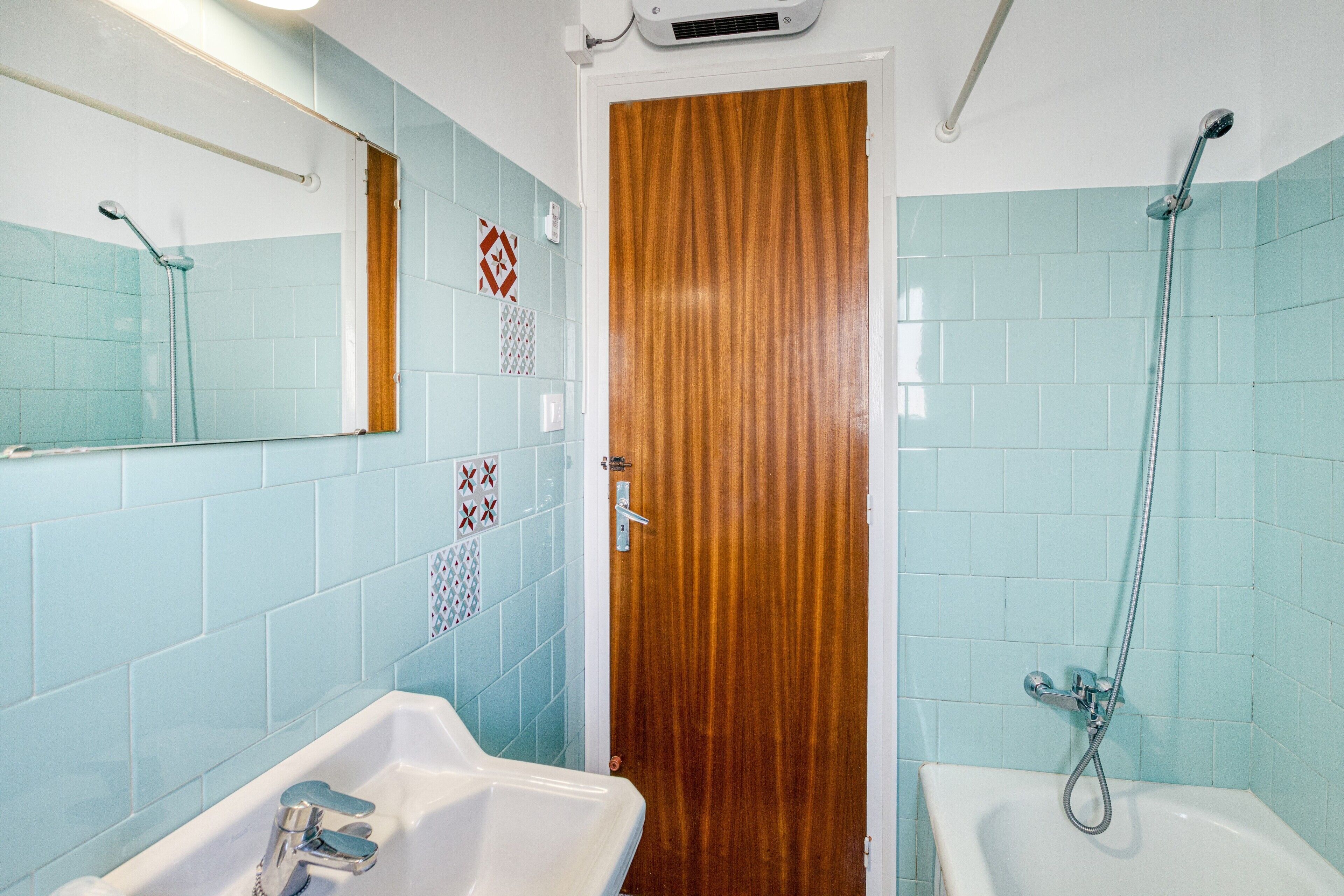 Un baño con ducha, lavamanos y puerta de madera.