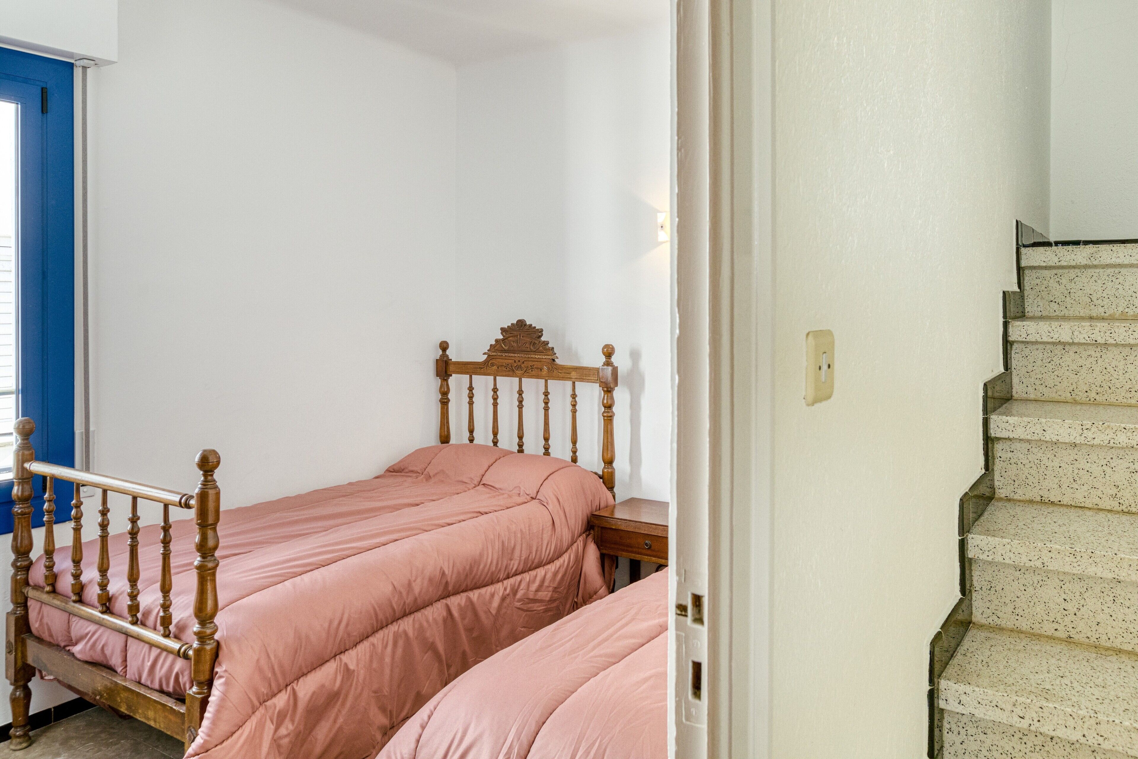 Een slaapkamer met twee enkele bedden, een houten hoofdbord, een witte muur en een trap.