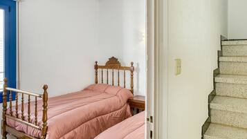 Een slaapkamer met twee enkele bedden, een houten hoofdbord, een witte muur en een trap.