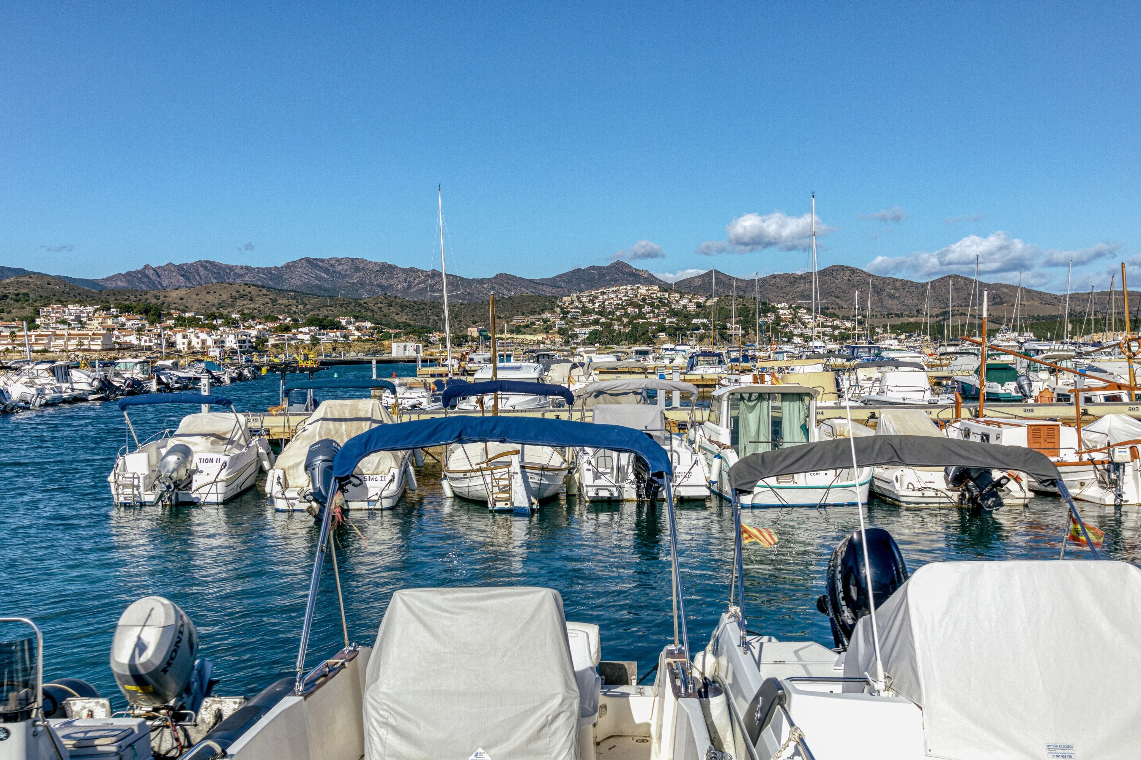 A marina with boats docked, a clear sky, and a town in the background.