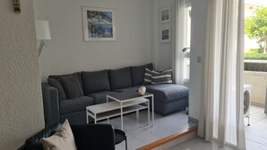 En moderne stue med en grå sofa, et hvidt sofabord og en sort lænestol. Der er et billede på væggen og et vindue med gardiner.
