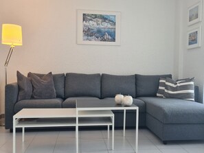 Een moderne woonkamer met een grijze bank, een witte salontafel en een schilderij aan de muur.