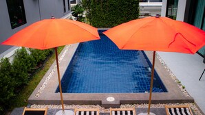 A swimming pool with two orange umbrellas, surrounded by four striped lounge chairs. - Hua-Hin Private pool villa (Tambon Hin Lek Fai, Amper Hua-Hin)