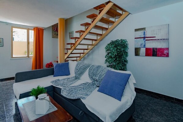A modern living room with a sofa, a coffee table, a staircase, and a plant.