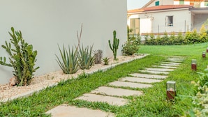 Een pad dat naar een gebouw met een witte gevel leidt, omgeven door groen gras en diverse planten.