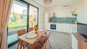 Een moderne keuken met een groot raam, een eethoek met rieten stoelen en een televisie op een houten kast.