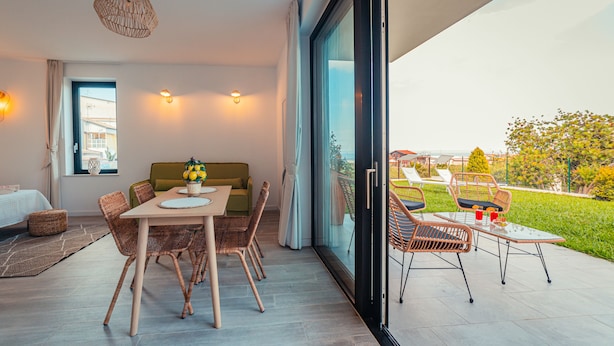 Een moderne woonkamer met een bank, een eettafel, stoelen, een groot raam en uitzicht op het groen.