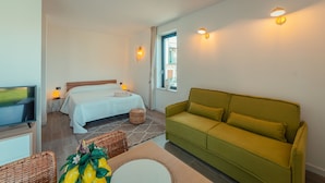 Een slaapkamer met een bed, een groene bank, een televisie en wandlampen.