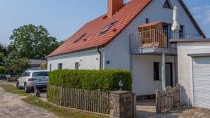 A two-story house with a red-tiled roof, a balcony, and a car parked in front. - 5 star FeWo Boddenblick (Glowe)