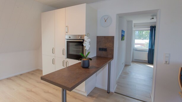 A modern kitchen with white cabinets, a built-in oven, a wooden countertop, and a potted orchid. - 5 star FeWo Boddenblick (Glowe)
