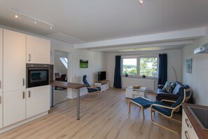 A modern, well-lit living room with a dining area, a sofa, and a TV. - 5 star FeWo Boddenblick (Glowe)