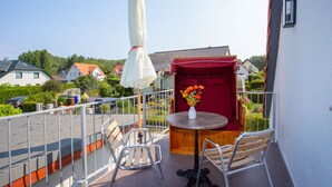 A balcony with a table, chairs, a white umbrella, and a vase of flowers. - 5 star FeWo Boddenblick (Glowe)