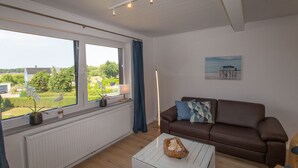 A living room with a brown sofa, a white coffee table, and a view of greenery outside. - 5 star FeWo Boddenblick (Glowe)
