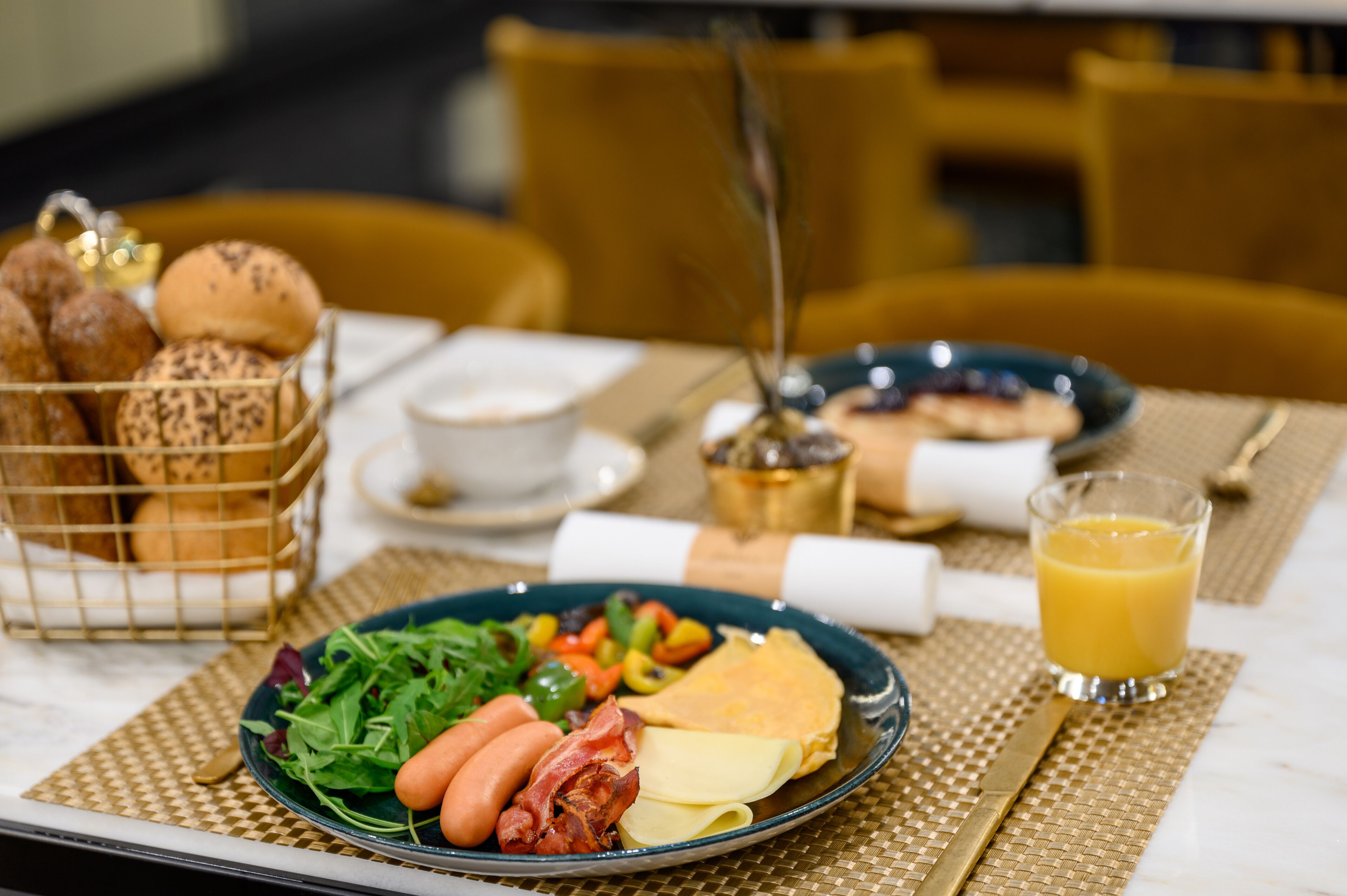 A breakfast setting with a plate of food, a basket of bread, a glass of orange juice, and a cup of coffee.