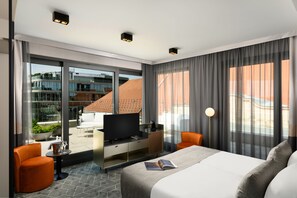 A modern hotel room with a large bed, a television, a desk with a coffee machine, and a view of the city through large windows. - Emerald Hotel (Budapest)