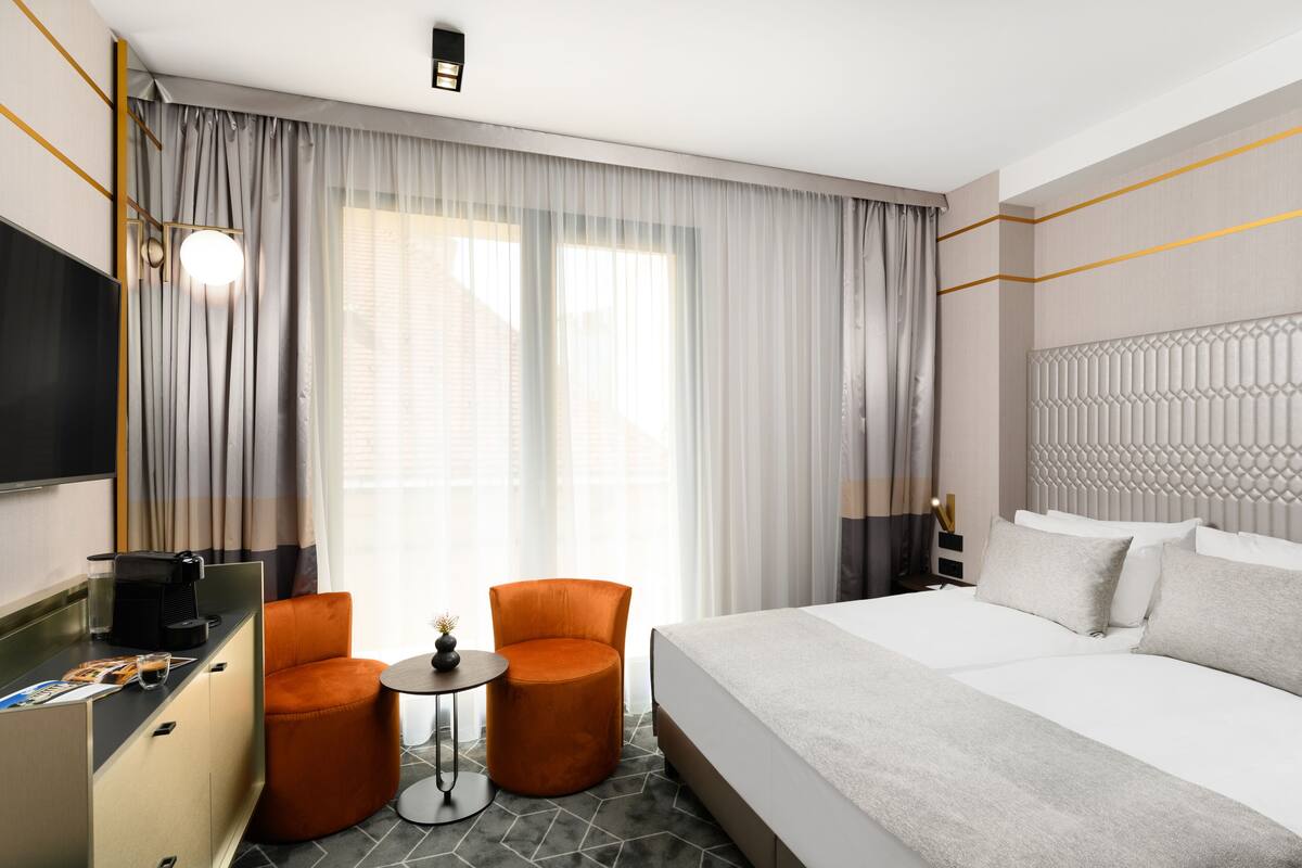 A hotel room with a bed, a desk, a chair, and a small table.