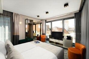 A modern hotel room with a large bed, a TV, a desk, and a view of the city. - Emerald Hotel (Budapest)