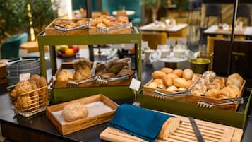 Un bufé con diversos panes y pasteles, incluyendo croissants y barras, dispuesto sobre tablas de madera y en cestas.